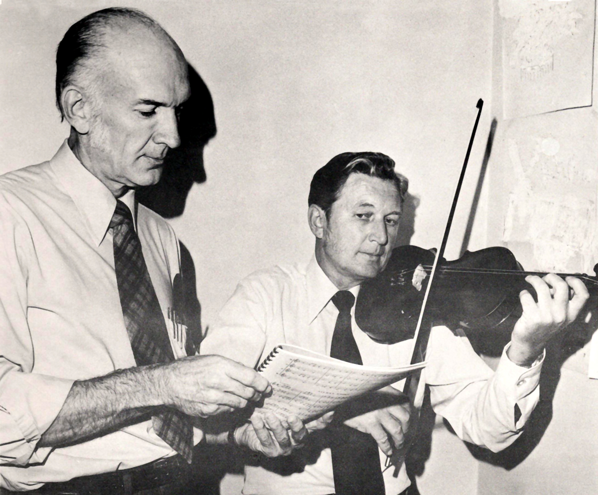 Two men, one holds sheet music and one plays a violin.