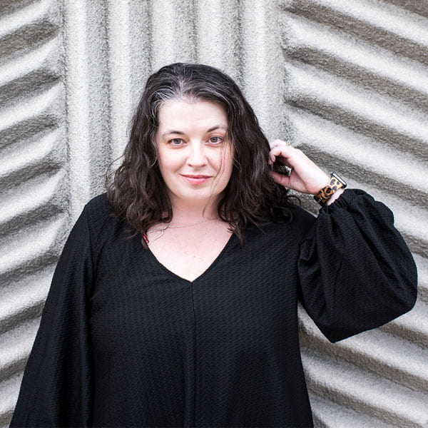 A woman with long black hair and a black blouse in front of a textured cement structure