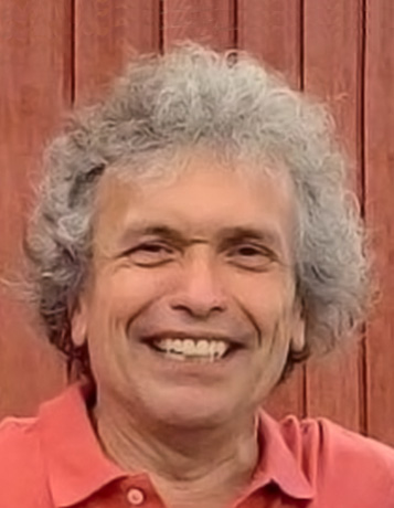A mature caucasian man with curly gray hair and a coral polo shirt smiles widely.
