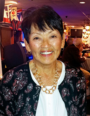 A mature smiling woman with asian features and short black hair at an event in a bar.