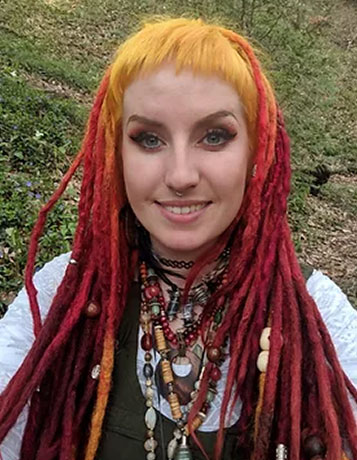 A selfie of a young caucasian woman with bright red dreds, short yellow fringe and lots of beads