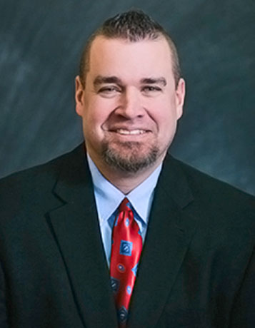A professional photo of a caucasian man with dark hair, a goatee, suit and tie
