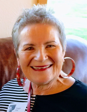 mature smiling Caucasian woman with very short gray hair and a black and white shirt and large hoop earrings.