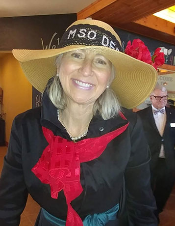 a middle-aged caucasian woman at an event wearing a large floppy hat with MSO Derby written on the band